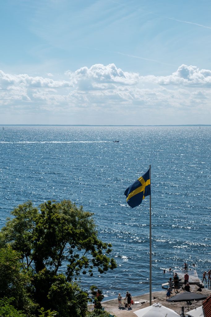 A beautiful view of the Swedish coastline with a Swedish flag waving over the ocean.