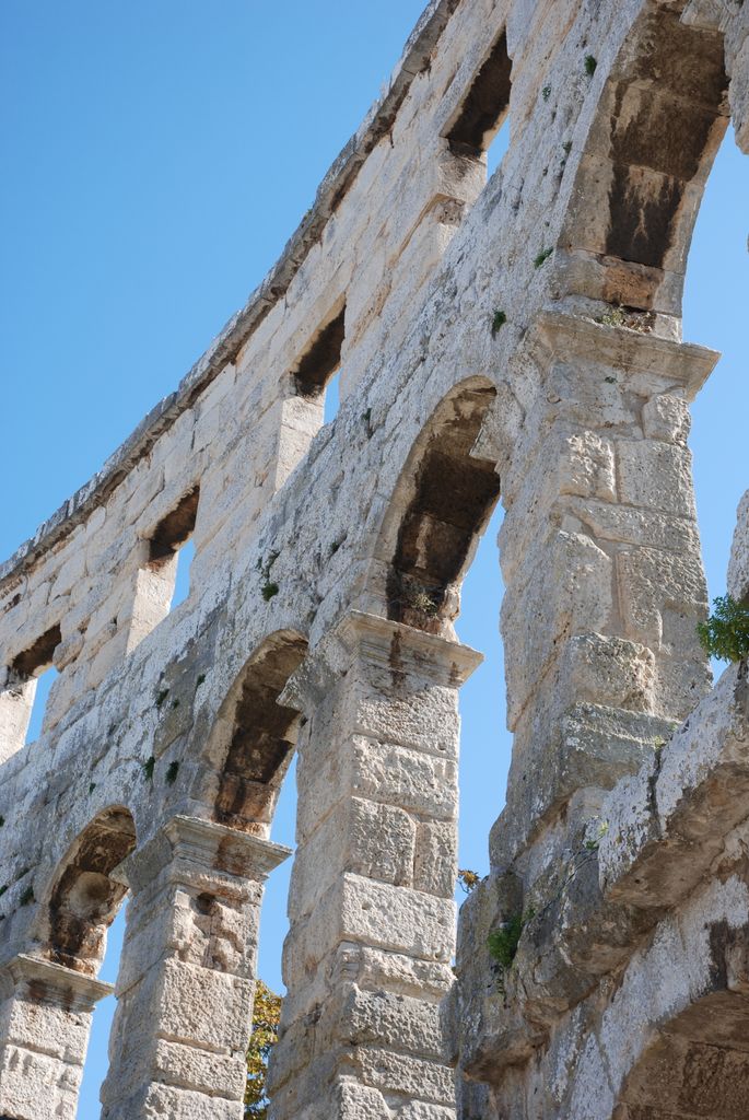 Close-up of the ancient Roman amphitheater arches in Pula, Croatia under a clear blue sky. Pula instagram captions